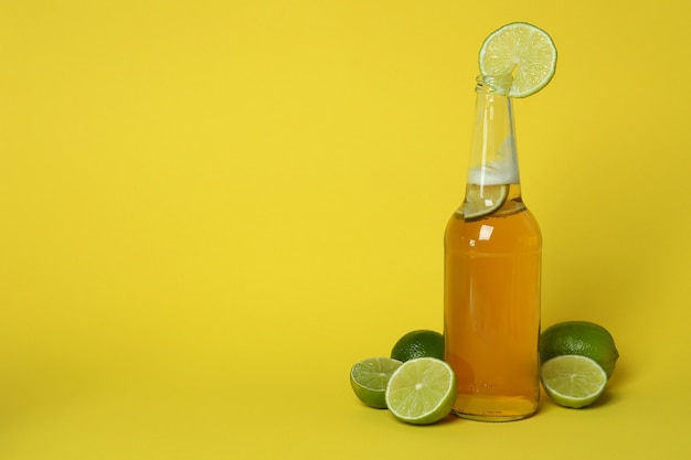 Bottle of beer and limes on yellow