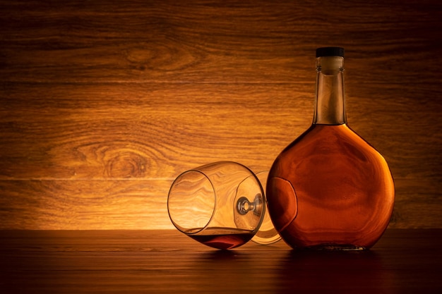 Photo bottle of brandy with wine glass on wooden background. cognac on the table