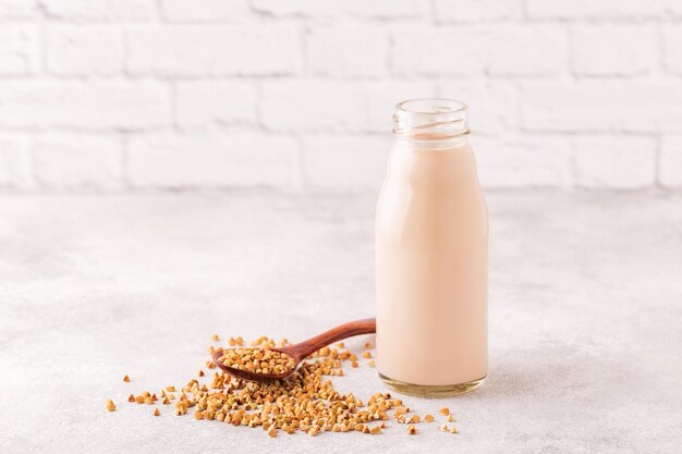 Una bottiglia di latte di grano saraceno e grano saraceno crudo su sfondo chiaro