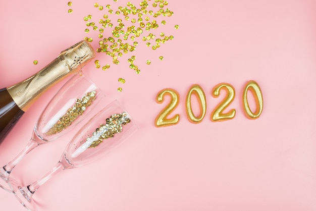 bottle of champagne, clear glasses with gold confetti and gold numbers on a pink pastel 