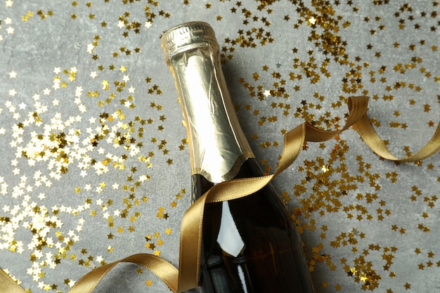 Bottle of champagne, glitter and ribbon on gray texture background.