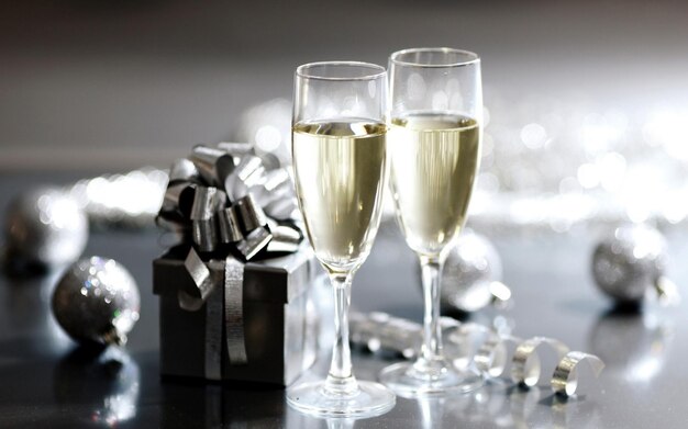 бутылка шампанского рядом со стопом подарков с подарком, упакованным в серебро