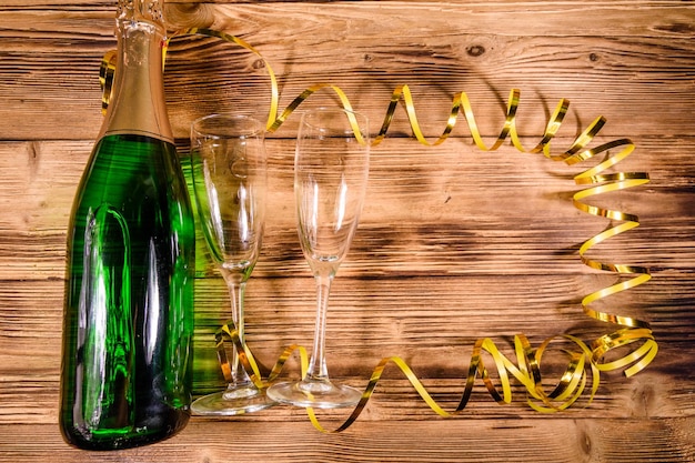 Photo bottle of champagne and two wineglasses decorated with golden ribbon on wooden table top view