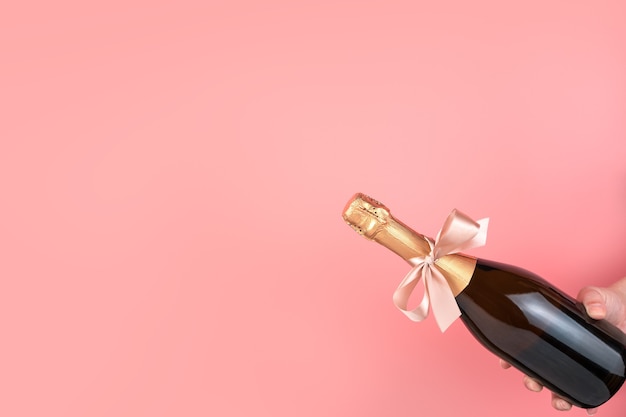 A bottle of champagne with a bow on a pink background