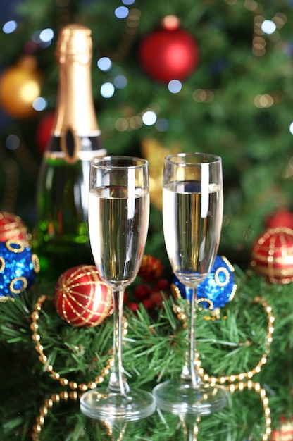 Бутылка шампанского с бокалом и елочные шары на фоне елки