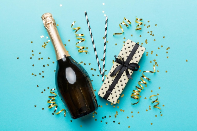 Bottle of champagne with glasses and colorful confetti on colored background. top view flay lay.