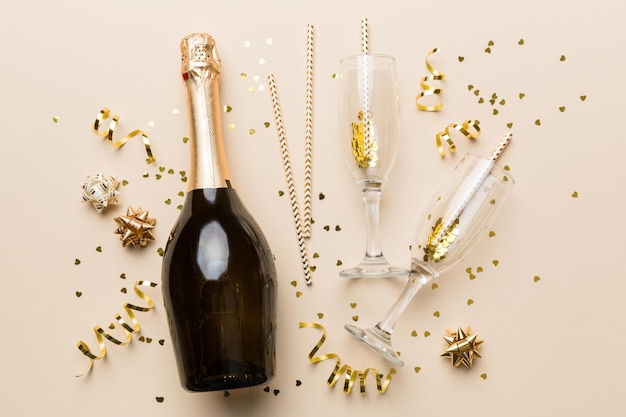 Bottle of champagne with glasses and colorful confetti on colored background top view flay lay