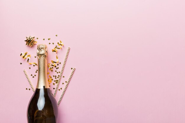 Bottle of champagne with glasses and colorful confetti on colored background top view flay lay