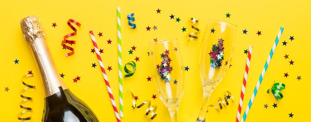 bottle of champagne with glasses and colorful confetti on colored background top view flay lay