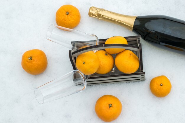 A bottle of champagne and a wooden box with tangerines in the snow.