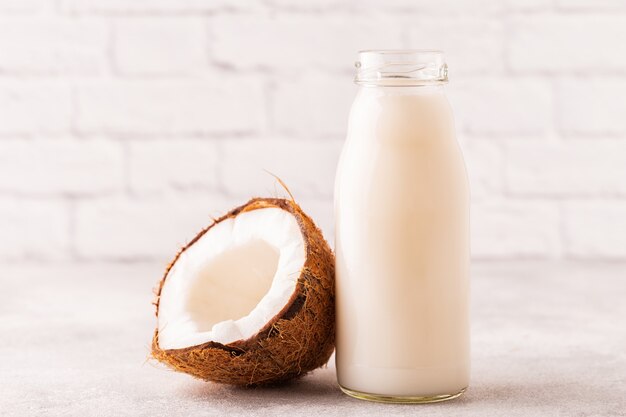 A bottle of coconut milk and coconut on a light background.