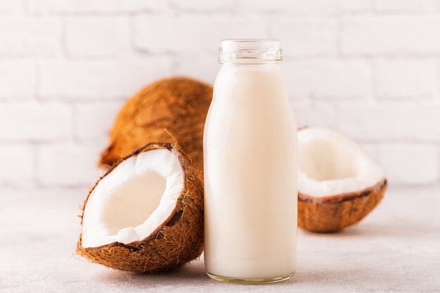 Una bottiglia di latte di cocco e cocco su uno sfondo chiaro.