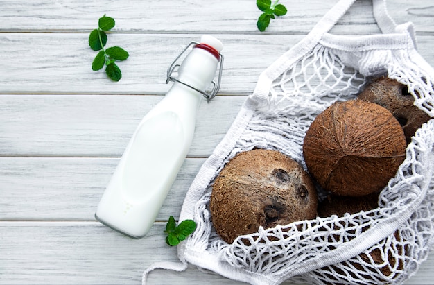 Bottiglia di latte di cocco e noci di cocco in un sacchetto a rete ecologica su un tavolo di legno