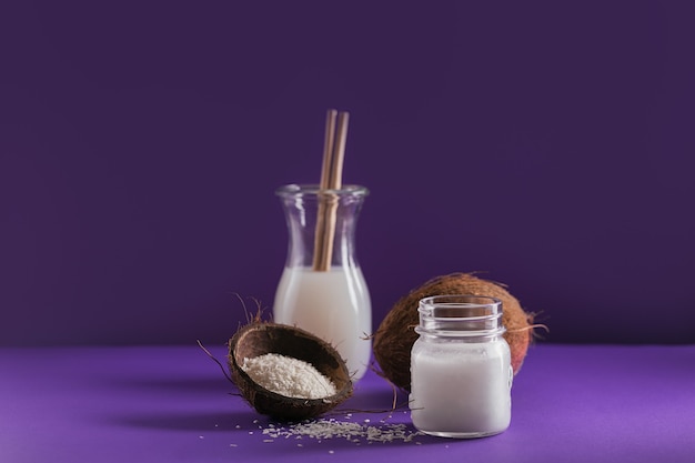 Bottle of coconut vegan milk, coco oil, whole coconut and flakes on violet