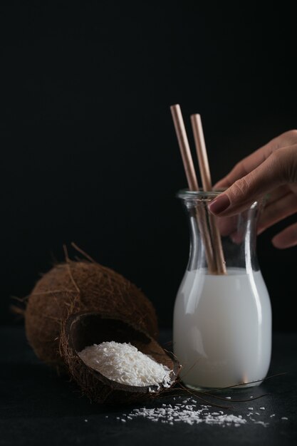 Bottle of coconut vegan milk with straws, whole coconut and flakes on a black background. Healthy lifestyle concept.