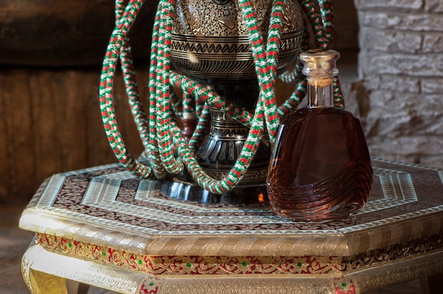 Foto una bottiglia di cognac e un narghilè su un antico tavolo decorativo riccamente decorato