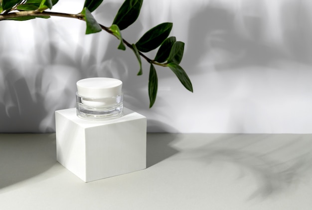 Bottle of cosmetic cream in sunlight with shadows of leaves