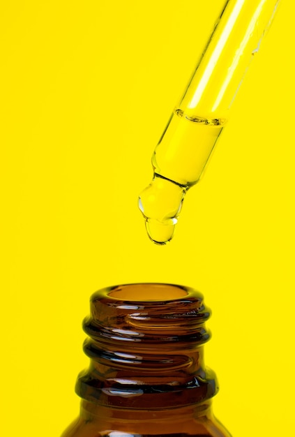 Bottle of cosmetic oil with a pipette on a yellow background. Close up liquid drop dripping. Beauty, medicine and  health care concept. Macro photo. Natural, eco cosmetics.