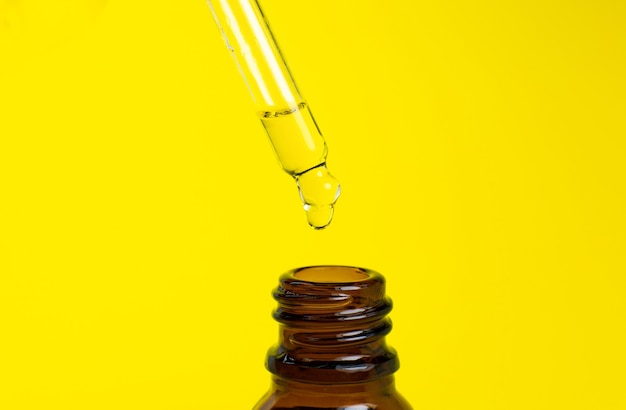 Bottle of cosmetic oil with a pipette on a yellow background. Close up liquid drop dripping. Beauty, medicine and  health care concept. Macro photo. Natural, eco cosmetics.