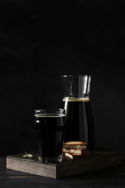 A bottle of dark beer and a glass of beer on a table with a black background.