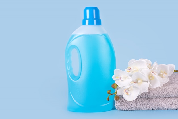 Bottle of detergent with clean towels and flowers on blue background