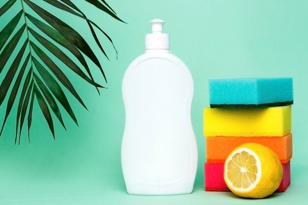 Bottle of dishwashing liquid sponges and lemon on color background