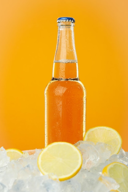 Bottle of drink in ice with lemon slices on orange background