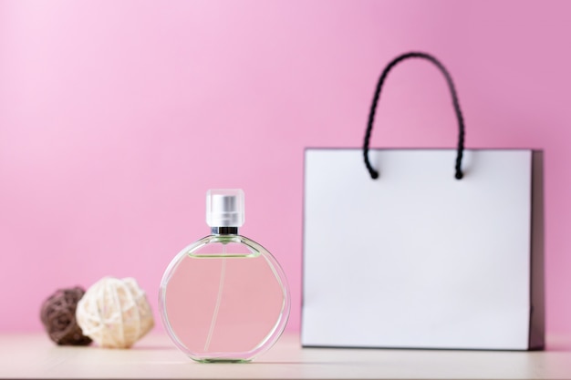 Bottiglia di profumo femminile preferito e un sacchetto di carta regalo su uno sfondo rosa