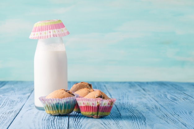 Bottle filled with fresh milk on blue wooden table with muffins