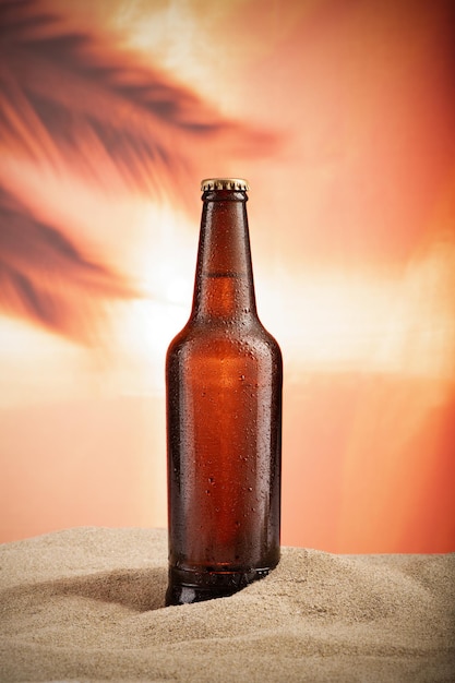 A bottle of fresh beer backlit at sunset on a sandy beach. Close up