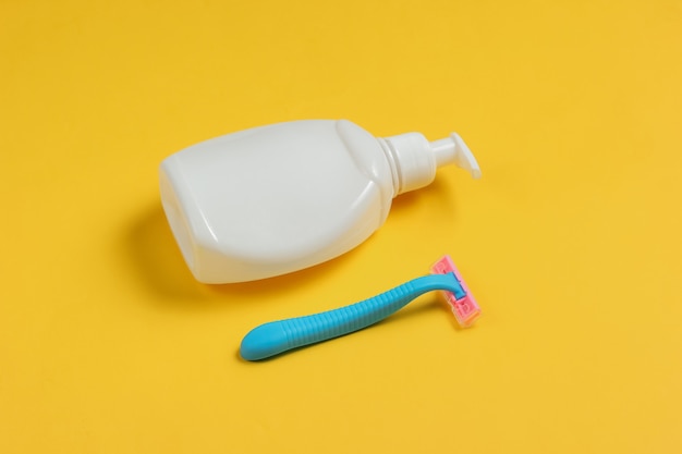 Bottle of gel for depilation, razor on yellow paper