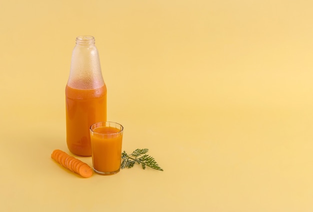 A bottle and a glass of carrot juice next to the chopped carrots