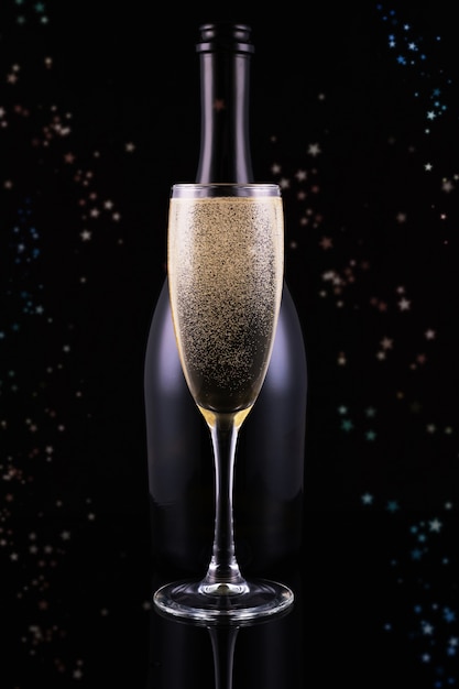 Bottle and glass of champagne with golden bokeh circles. Place for text. Festive concept.