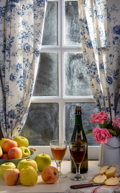 Bottle and glass of cider with apples. In rustic house