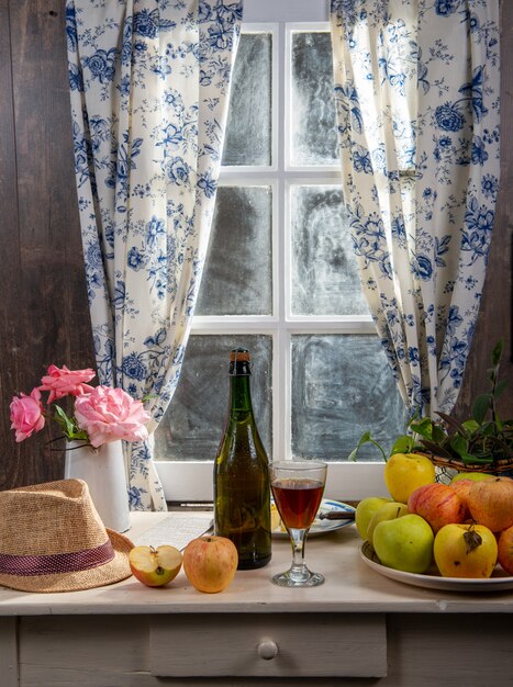 Bottle and glass of cider with apples. In rustic house