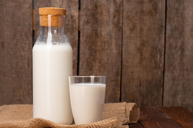 Photo bottle and glass of milk on wooden table close up