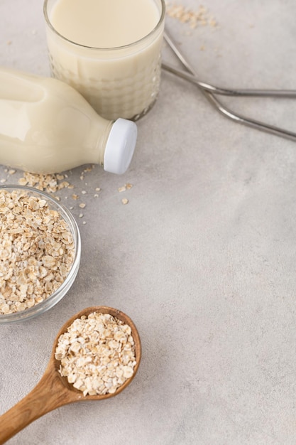 A bottle and a glass of plantbased oat milk with an ingredient in a bowl with reusable straws on a light background