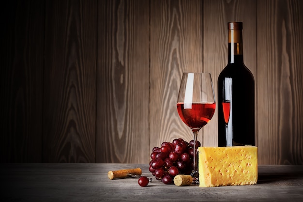 Bottle and glass of red wine with cheese grapes and corkscrew