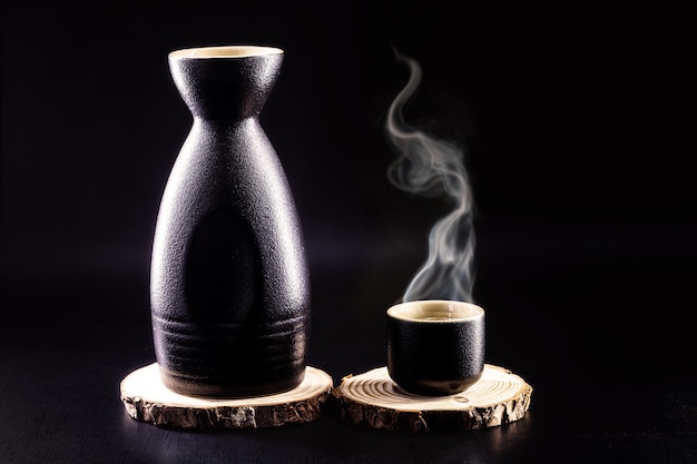 bottle and glass of sake, hot Japanese alcoholic drink, with steam, black background and copy space