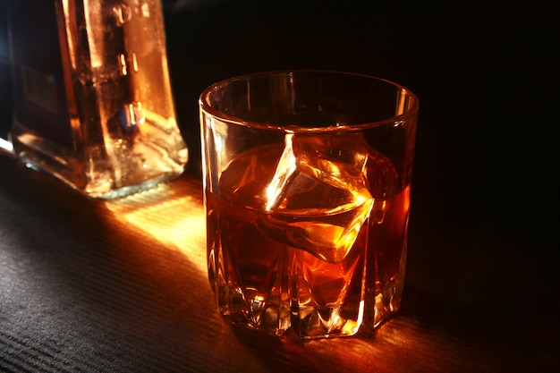 Bottle and Glass of whiskey or bourbon with ice on black stone table.