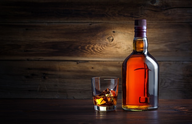 Bottle and glass of whiskey with ice on a wooden background