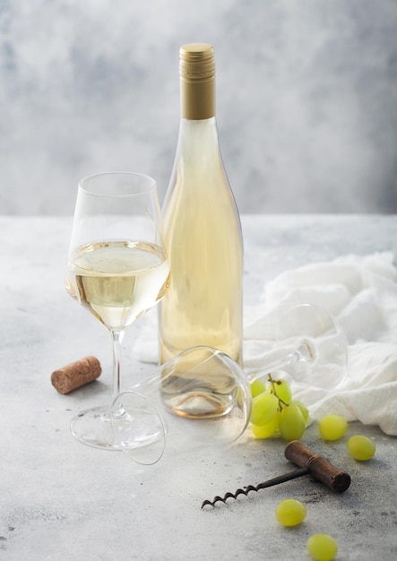 Bottle and glass of white homemade wine with grapes and corkscrew with linen cloth on light table background