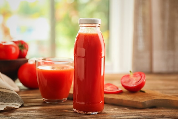 bottle and glass with fresh tomato juice on table indoors