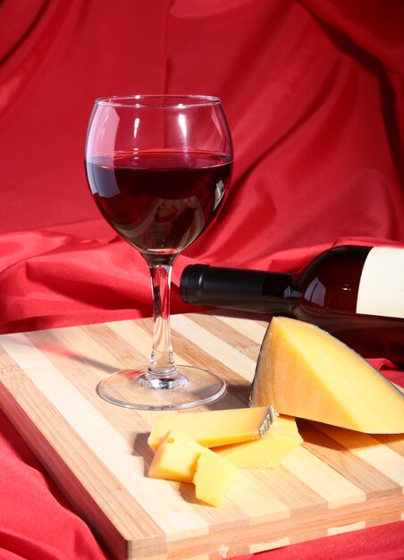 Bottle and Glass with red wine grapes and chees on wooden table.