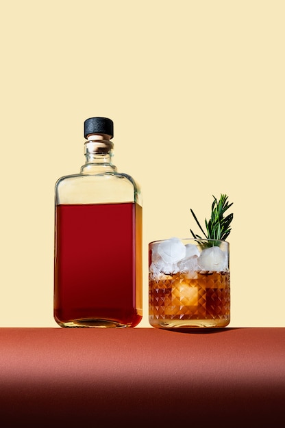 Bottle and Glass with Whiskey and Ice on Brown Table on Light Background. Modern Style. Creative Concept