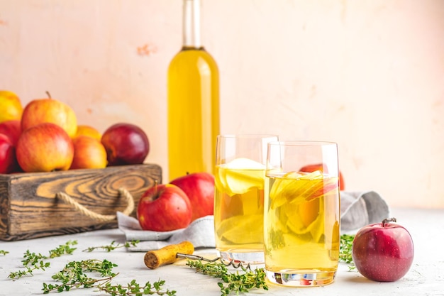 Bottle and glasses of homemade organic apple cider with fresh apples in box light concrete table surface shallow depth of the field