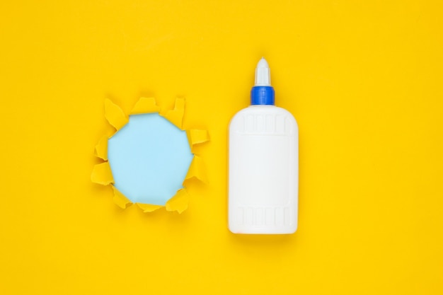 Bottle of glue on yellow paper with torn hole