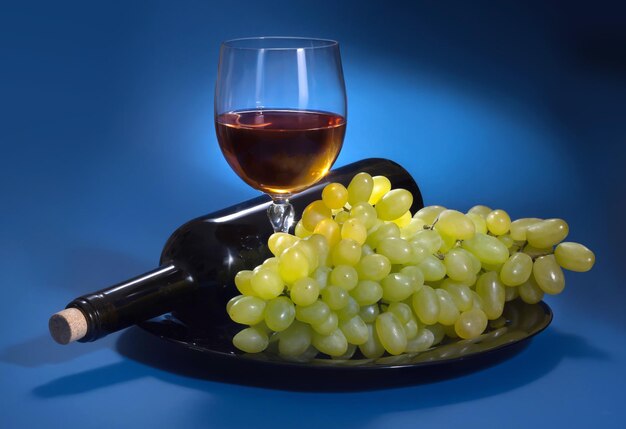 A bottle of grape wine and white grapes on a blue background