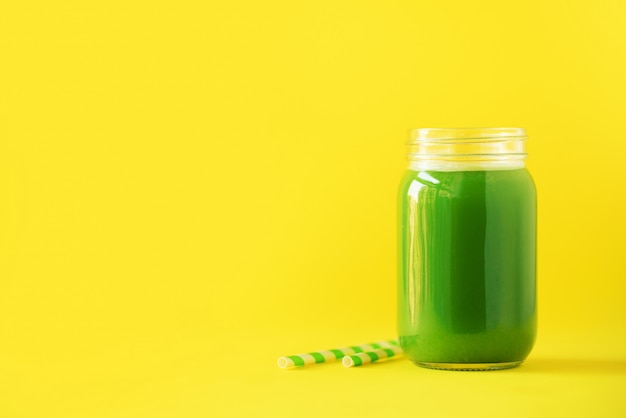 Bottle of green celery smoothie on yellow background