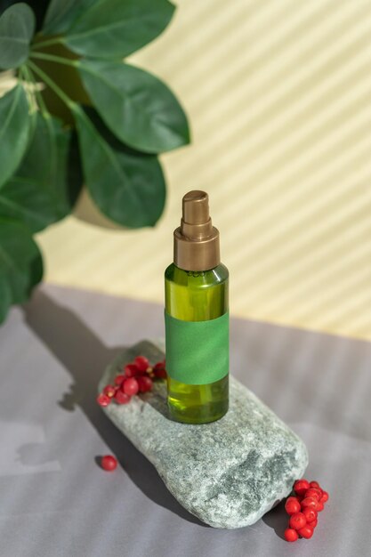 A bottle of green color with a spray bottle lies on the stones, next to the green leaves and berries